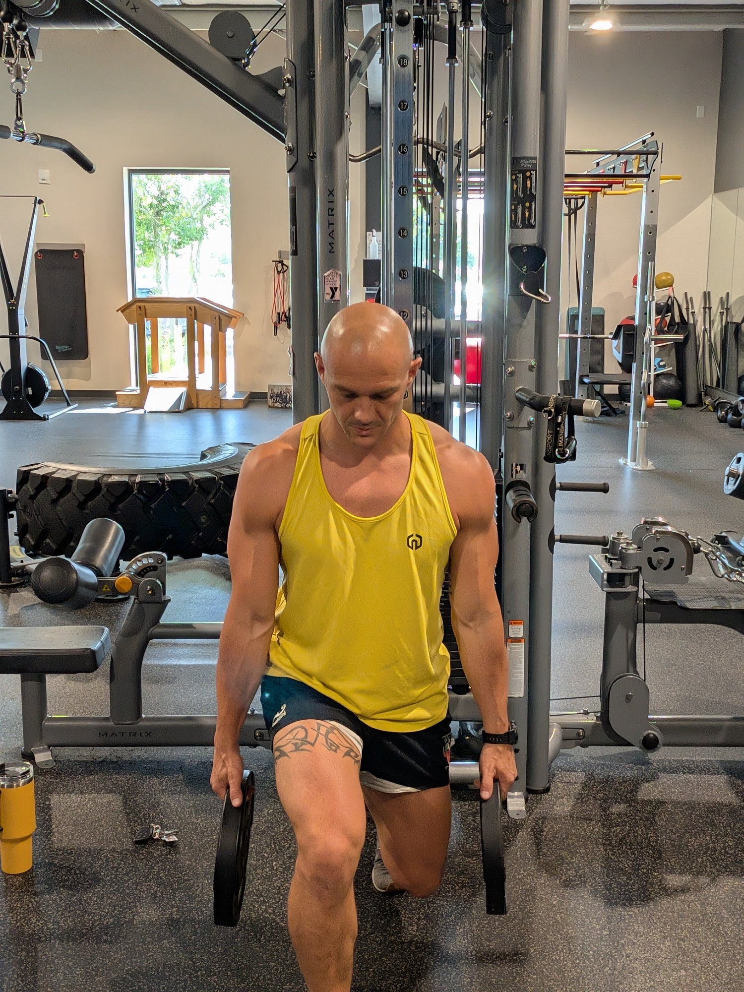 Man in yellow tank top and black shorts exercising with resistance bands in a gym.